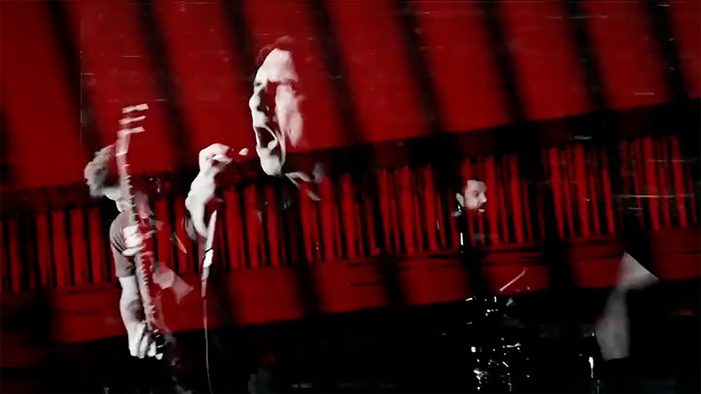 A singer screaming into a microphone over a red and black collage in the IGNITE music video for The River